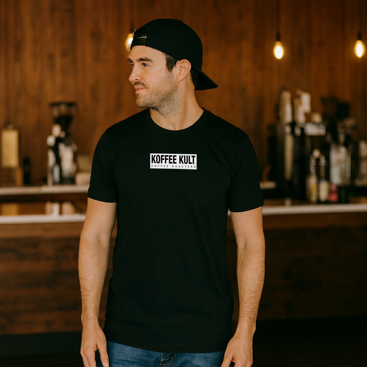 Man wearing a black t-shirt with 'Koffee Kult' logo in a bar setting