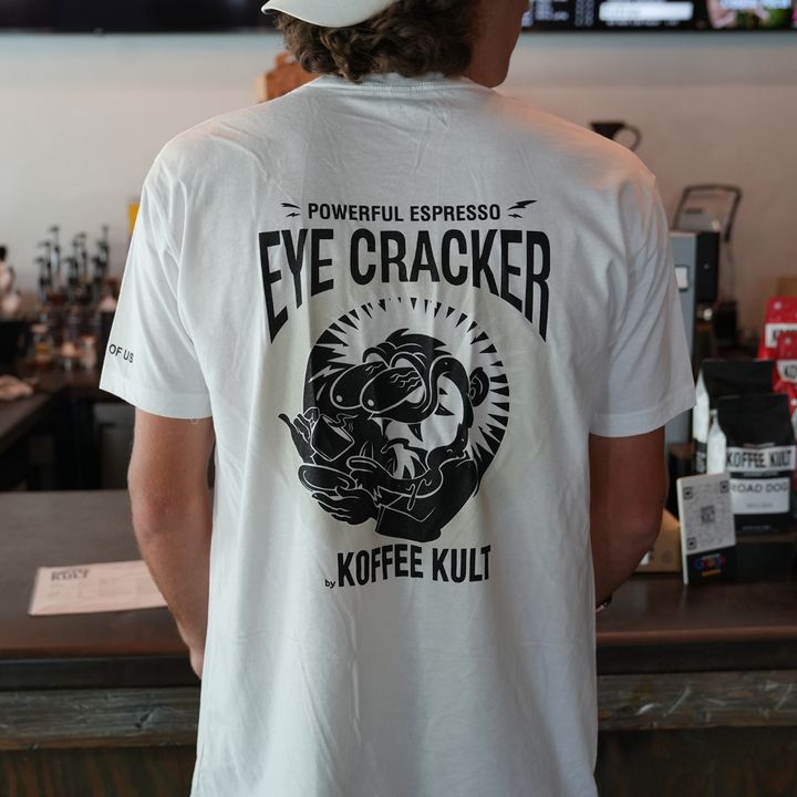 Person wearing a white t-shirt with 'Eye Cracker' design and text in a coffee shop setting