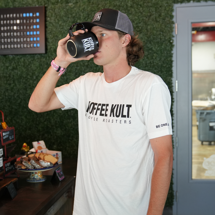 Person wearing a 'Coffee Kult' t-shirt and drinking from a coffee cup.