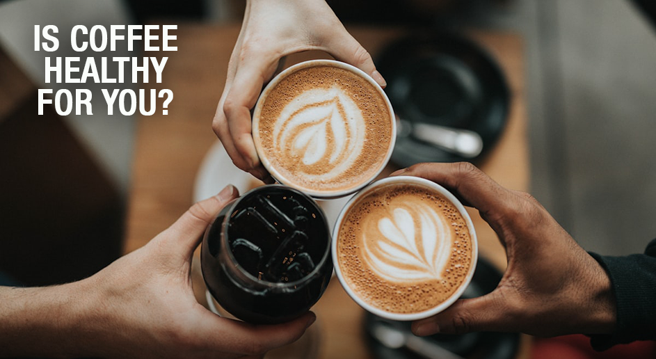 Two hands holding cups of coffee with latte art, one black and one with a leaf design, on a wooden table.