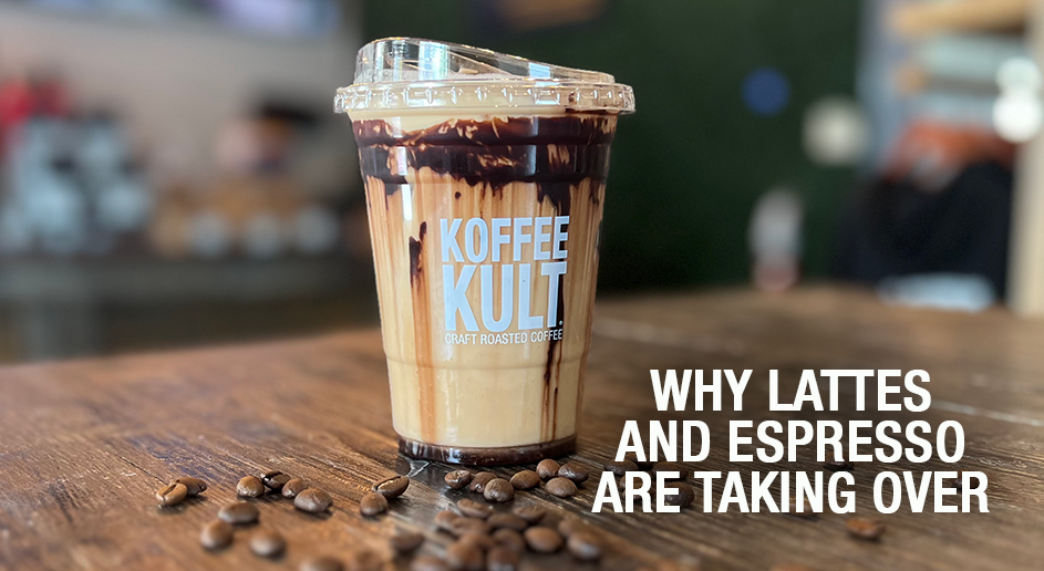 A clear plastic cup of layered latte with chocolate drizzle and visible Koffee Kult branding, sitting on a wooden table with coffee beans scattered around it. Large white text on the right reads, 'WHY LATTES AND ESPRESSO ARE TAKING OVER.