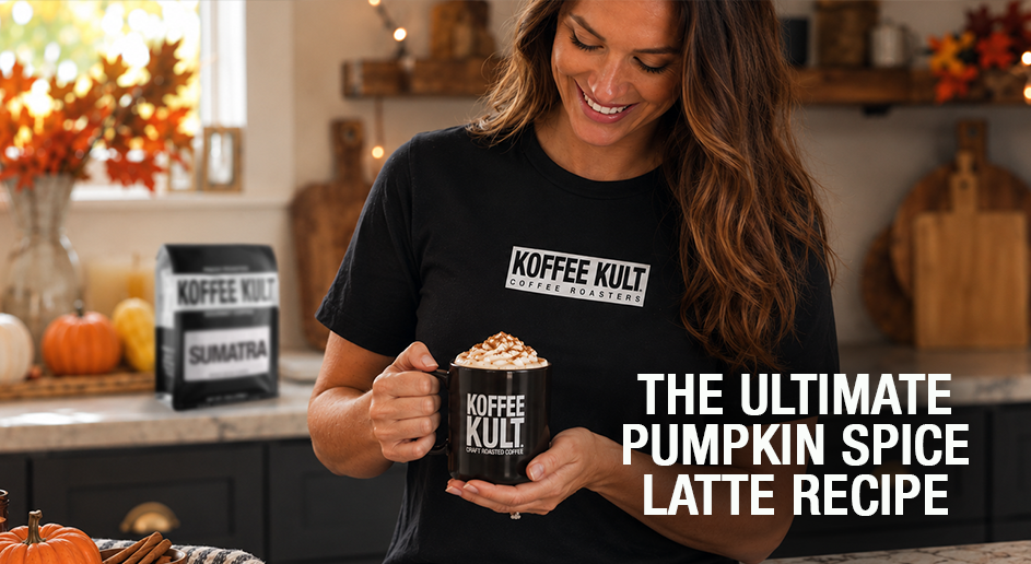 A woman in a kitchen setting wearing a black Koffee Kult t-shirt and holding a mug of pumpkin spice latte, with text overlay reading 'THE ULTIMATE PUMPKIN SPICE LATTE RECIPE'.