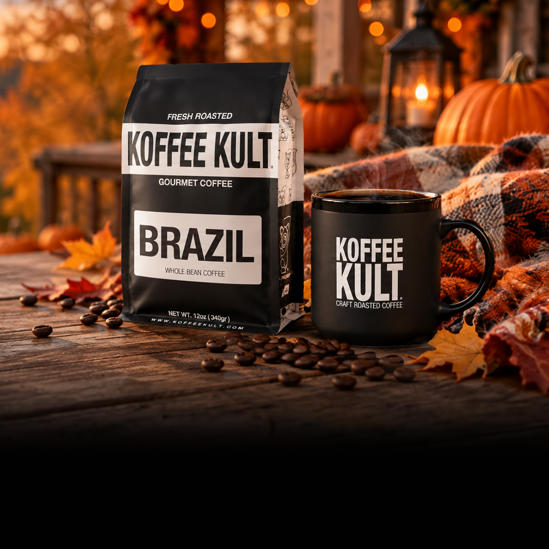 A bag of Koffee Kult Brazil gourmet coffee stands next to a matching black ceramic mug on a rustic wooden table, with scattered coffee beans, autumn leaves, a plaid blanket, and pumpkins in the background.