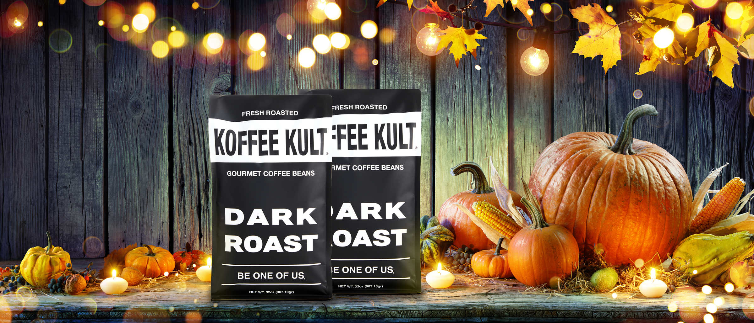 Two Koffee Kult coffee bags on a wooden surface with pumpkins and lights in the background.