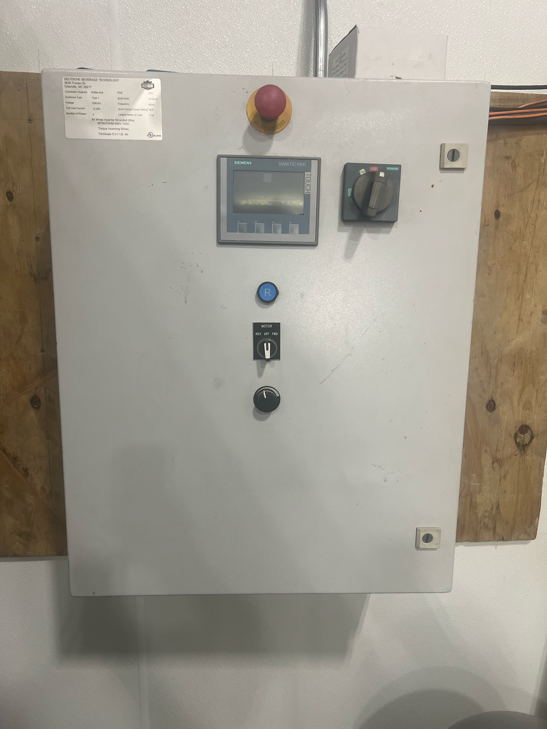 Control panel with various buttons and a display on a wooden wall.